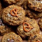 A stack of healthy cowboy cookies with visible oats, chocolate chips, and crushed pretzels on a cooling rack.