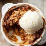 A single-serve ramekin of golden brown apple crisp with a buttery oat topping