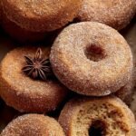 A plate of golden-brown gluten-free apple cider donuts coated in cinnamon sugar