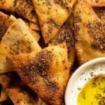 A bowl of golden brown, seasoned pita chips made in an air fryer with a side of hummus.