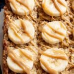 A square of golden brown baked oatmeal with peanut butter and banana on a white plate