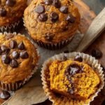 A batch of golden pumpkin protein muffins with dark chocolate chips on a wire rack.
