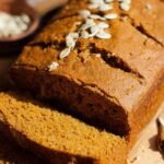 A golden loaf of healthy pumpkin bread on a wire cooling rack.