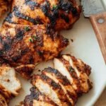 Golden brown grilled boneless chicken thighs with charred grill marks on a white platter
