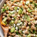 A colorful Mediterranean bean salad with chickpeas, tomatoes, cucumbers, and feta cheese in a white bowl.