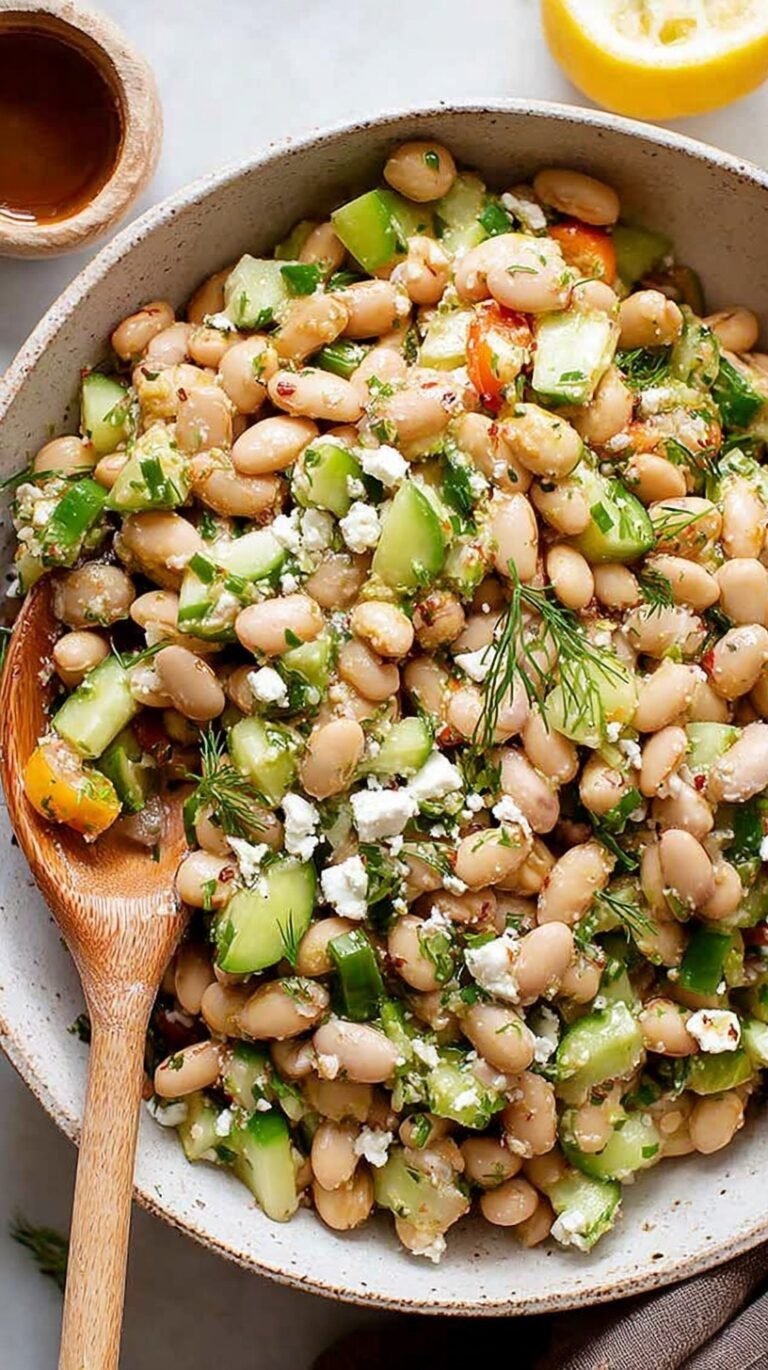 A colorful Mediterranean bean salad with chickpeas, tomatoes, cucumbers, and feta cheese in a white bowl.