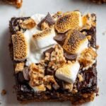 A stack of healthy s'mores brownies topped with toasted marshmallows and dark chocolate chips on a parchment-lined tray.