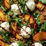 A platter of grilled peach halves with creamy burrata cheese and fresh arugula