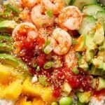 A colorful shrimp poke bowl with avocado, cucumber, and carrots over sushi rice.