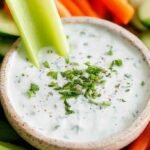 A bowl of creamy healthy homemade ranch dip surrounded by fresh carrot sticks and cucumbers