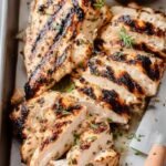 Grilled Greek yogurt marinated chicken breasts sliced on a wooden board with lemon wedges