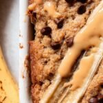 A warm mug containing a single serving of banana bread topped with a small pat of melting butter.