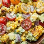 A colorful bowl of Summer Avocado Corn Salad with yellow corn, green avocado, and red tomatoes.