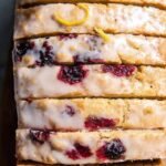 A sliced loaf of Lemon Blackberry Bread with a white citrus glaze and fresh berries.