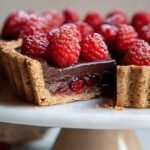 A decadent chocolate raspberry tart with fresh berries and dark chocolate ganache on a serving plate.