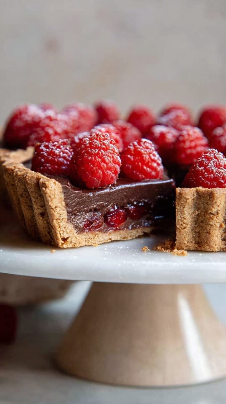 A decadent chocolate raspberry tart with fresh berries and dark chocolate ganache on a serving plate.