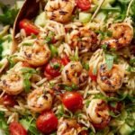 A bright Mediterranean shrimp orzo salad in a white bowl with fresh lemon and herbs.