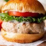 Four juicy grilled turkey burgers on a platter with fresh toppings and buns