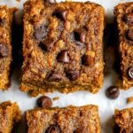 Golden brown pumpkin oatmeal bars with dark chocolate chips on a parchment-lined baking sheet.