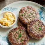Golden brown air fryer frozen sausage patties served on a white plate with scrambled eggs