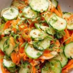 A bright and colorful bowl of julienned cucumbers and carrots tossed in a sesame dressing and topped with cilantro.
