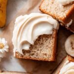 A square gluten-free banana cake on a wire rack being sliced for serving.