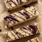 A stack of homemade nut-free protein bars with mini chocolate chips on a parchment-lined tray.