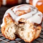 Golden brown cinnamon rolls with melting white cream cheese icing in an air fryer basket