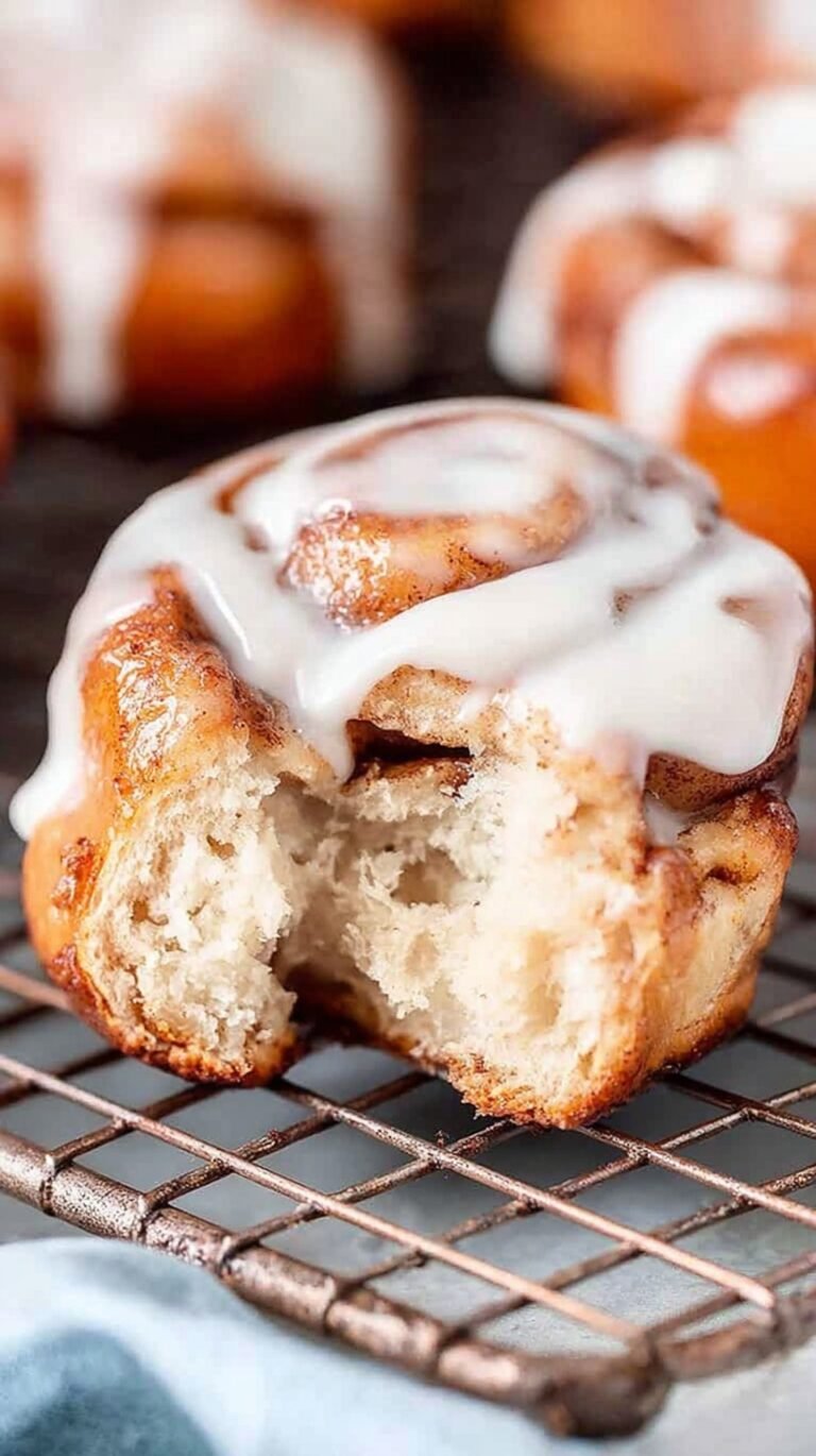 Golden brown cinnamon rolls with melting white cream cheese icing in an air fryer basket