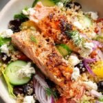 A vibrant Greek Salmon Quinoa Salad in a bowl with feta, olives, and cucumbers