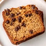 A sliced loaf of golden brown peanut butter bread on a wooden cutting board.
