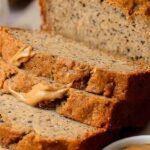 A sliced loaf of healthy peanut butter banana bread on a wire cooling rack.