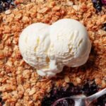 A golden brown gluten-free blueberry crisp in a white baking dish with bubbling purple berries.