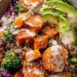 A colorful quinoa sweet potato bowl with black beans, kale, and avocado drizzled with tahini dressing.