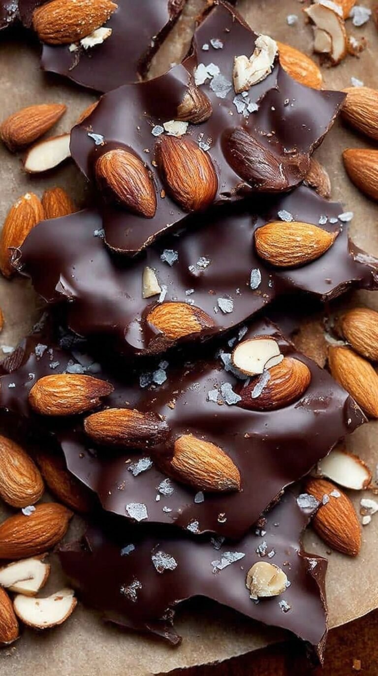 Pieces of dark chocolate almond bark with flaky sea salt on parchment paper