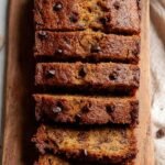 A golden brown loaf of oat flour banana bread sliced on a wooden board