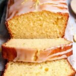 A golden loaf of healthy lemon pound cake sliced on a wooden board with fresh lemon zest on top.