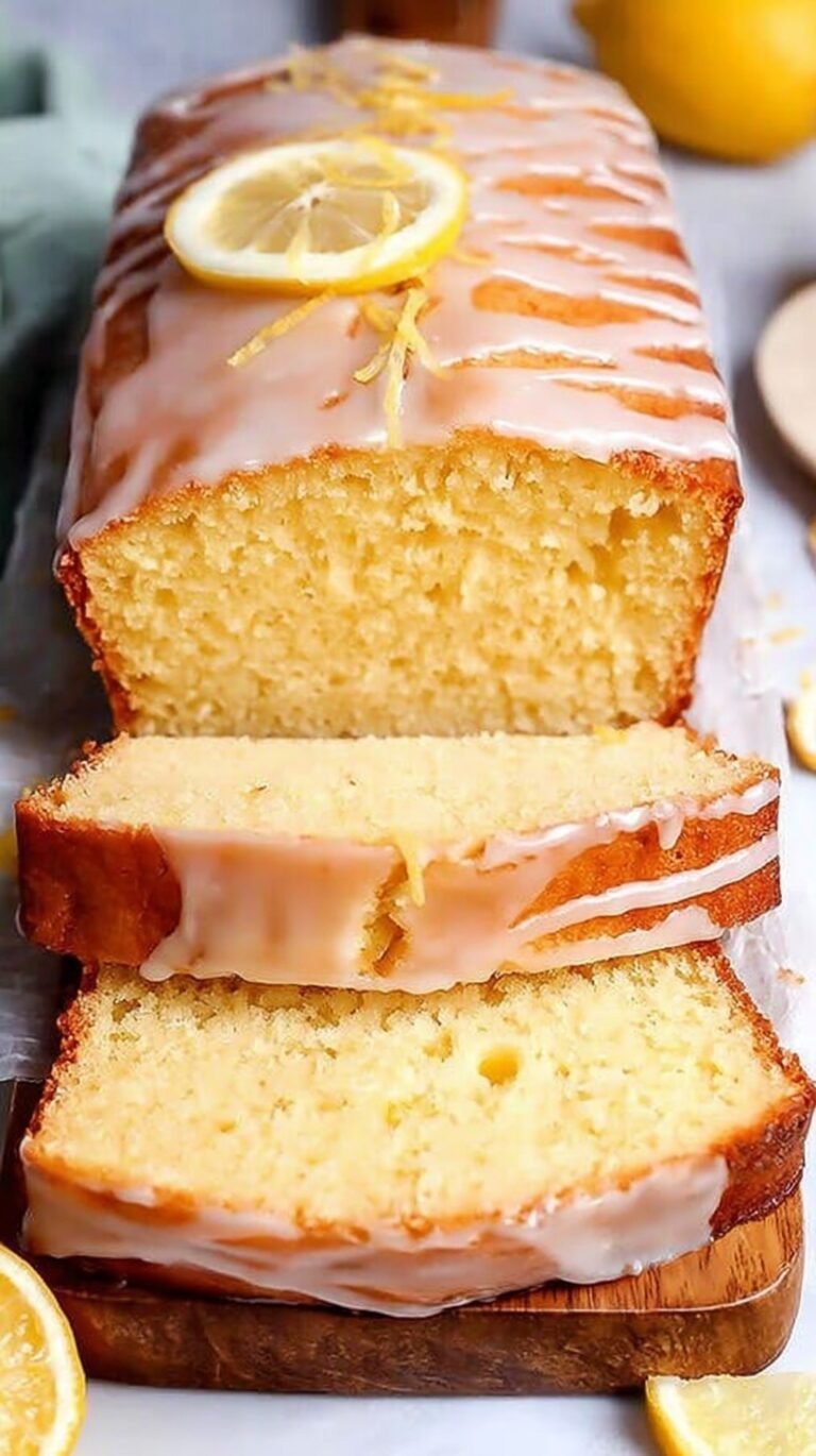 A golden loaf of healthy lemon pound cake sliced on a wooden board with fresh lemon zest on top.
