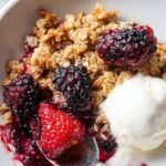 A warm healthy blackberry crumble in a baking dish with a golden oat and walnut topping.