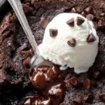 A gooey flourless brownie in a cast iron skillet with melted chocolate chips and crisp edges.