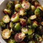 Roasted halved brussel sprouts coated in a glossy honey sriracha glaze on a baking sheet