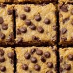 A stack of golden brown peanut butter chickpea blondies topped with melted chocolate chips on a white plate.