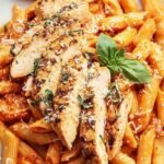 A bowl of whole wheat penne pasta in a creamy tomato vodka sauce with grilled chicken and fresh basil.