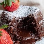 Two vegan molten lava cakes on white plates with gooey chocolate centers flowing out