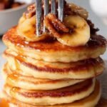 A stack of fluffy buttermilk pancakes topped with sliced caramelized bananas and a rich brown sugar sauce.