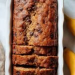 A golden brown loaf of dairy-free banana bread sliced on a wooden board.