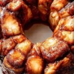 Golden brown vegan monkey bread pieces coated in cinnamon sugar and drizzled with white glaze on a platter