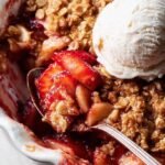 A golden brown strawberry apple crumble in a ceramic baking dish with bubbling fruit juices