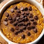 A single-serve ramekin filled with golden pumpkin baked oats topped with melted chocolate chips.