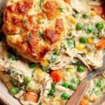 A white bowl filled with creamy chicken, carrots, and peas in a savory sauce garnished with fresh parsley.